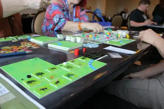 Players at a convention table building forests from green tree and animal tiles